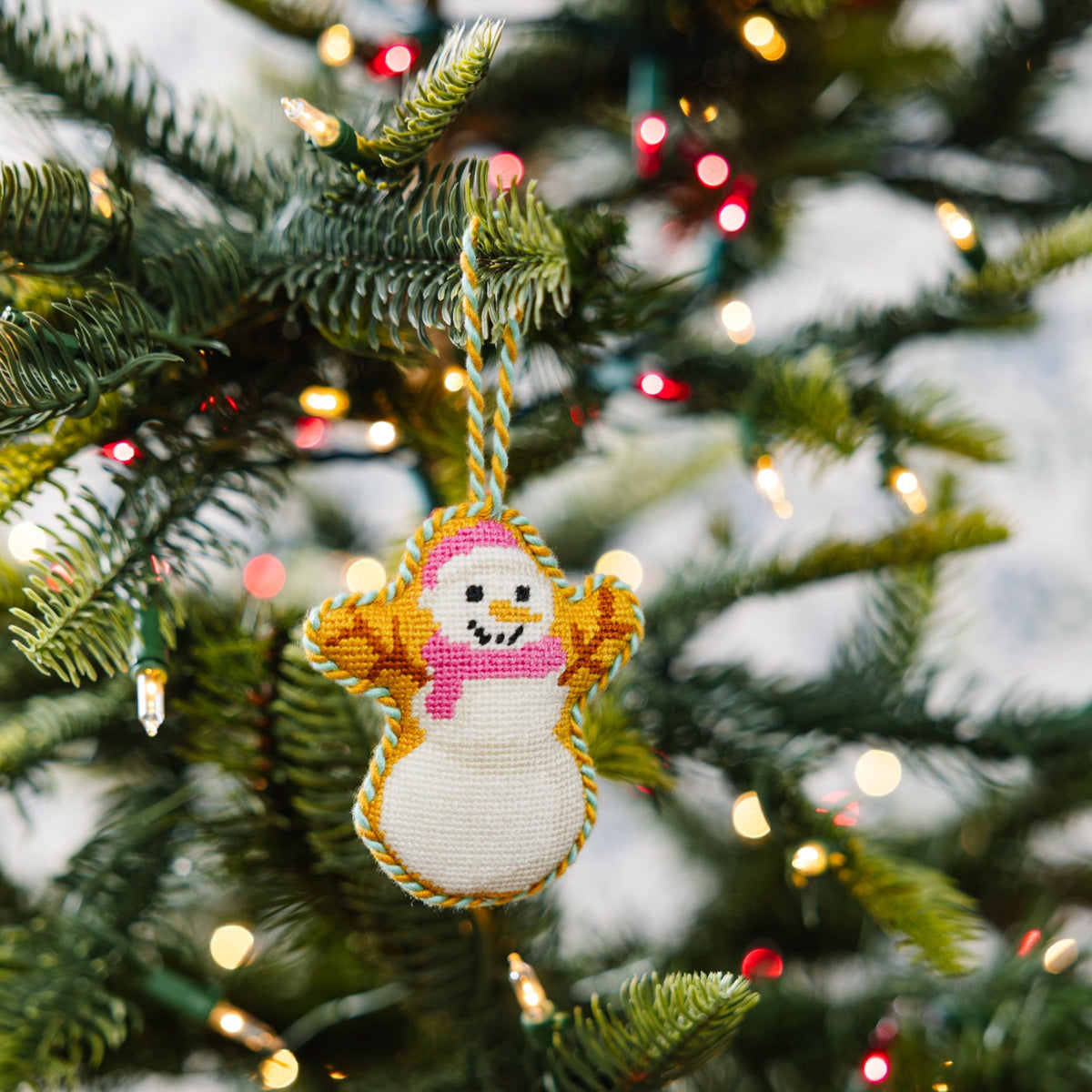 Hanging needlepoint snowman ornament with braided yarn hanger and stitched pink scarf