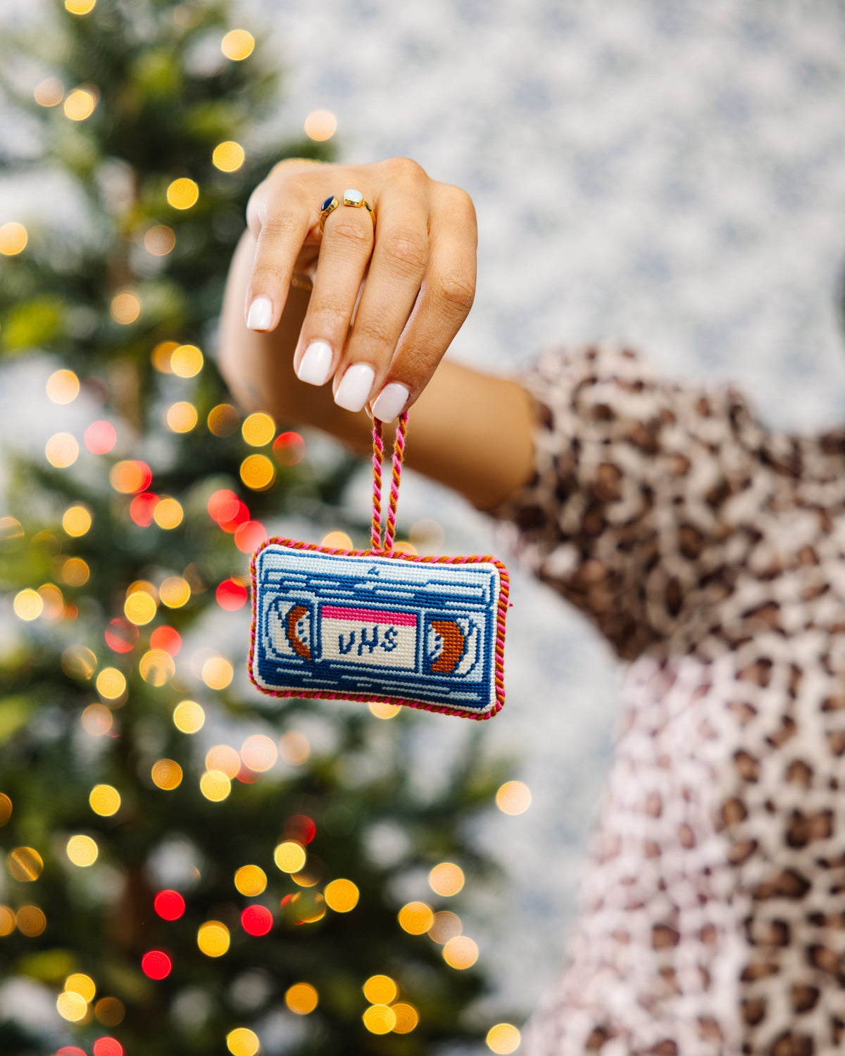 Needlepoint VHS tape ornament held by braided cord, blue and white stitched VHS label