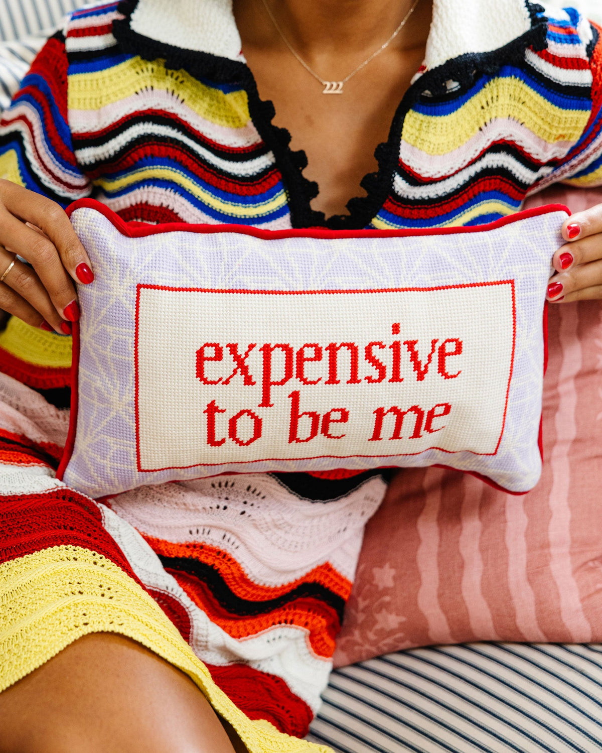 Needlepoint lumbar pillow with red “expensive to be me” text on off-white fabric