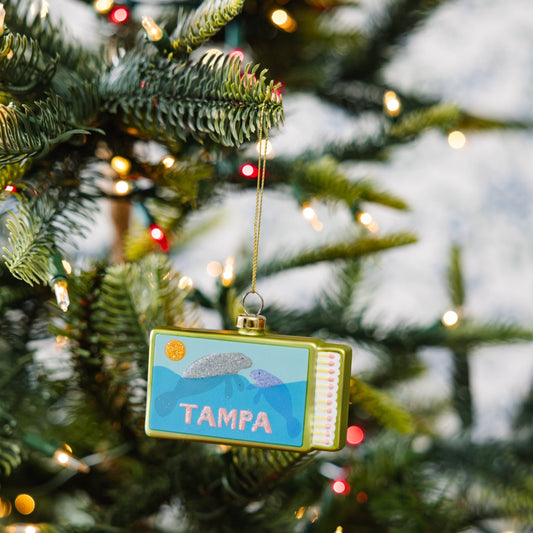 Tampa matchbook ornament with gold frame, hanging from a Christmas tree branch