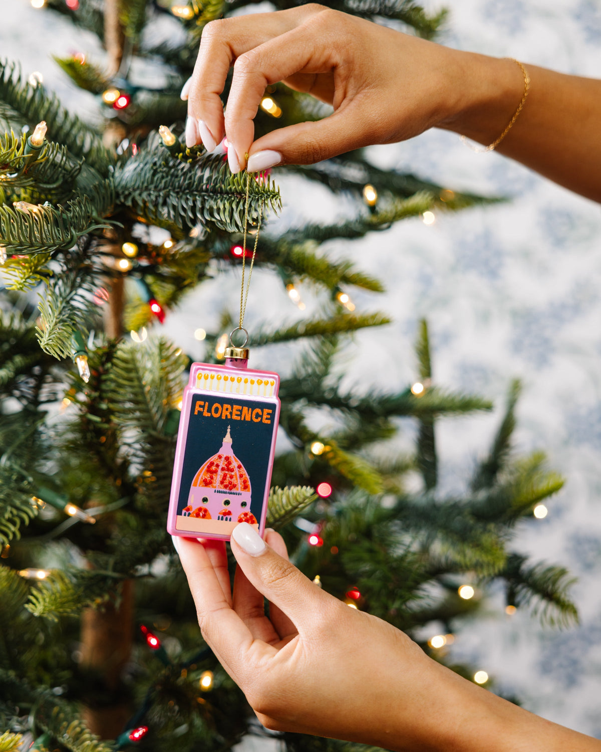 Florence matchbook ornament held by hands, pink with dome design and gold cord
