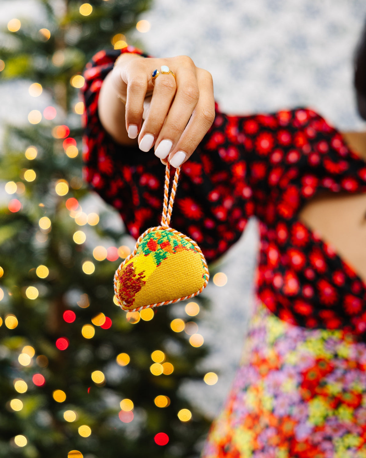 Hand holding a needlepoint taco ornament by its braided loop