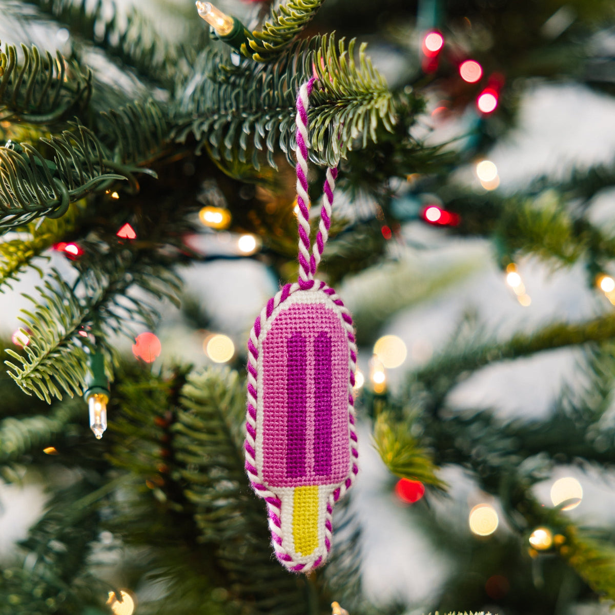 Needlepoint popsicle ornament hanging on Christmas tree branch, pink purple stripes and yellow