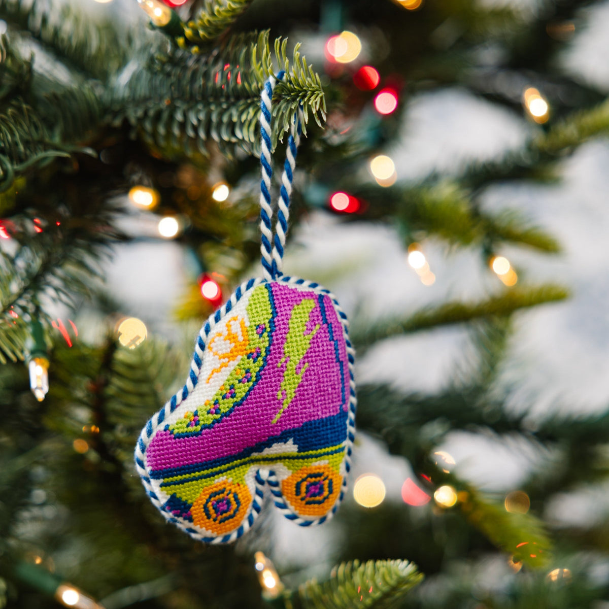 Needlepoint roller skate ornament in purple and pink, hanging from braided loop