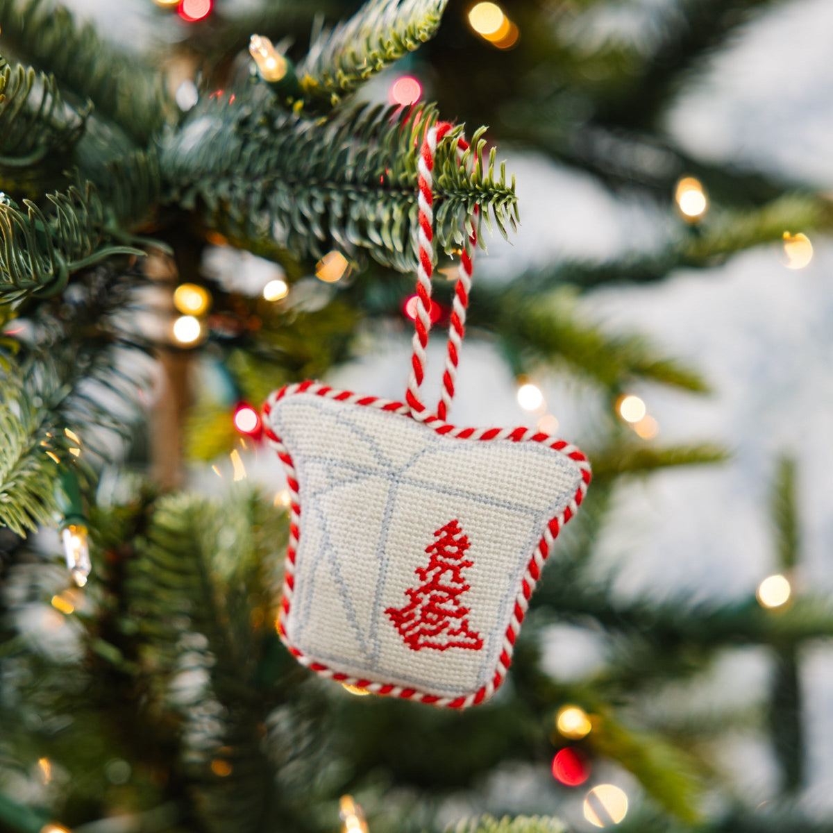 Beige needlepoint takeout box ornament with red stitched symbol and twisted hanging cord