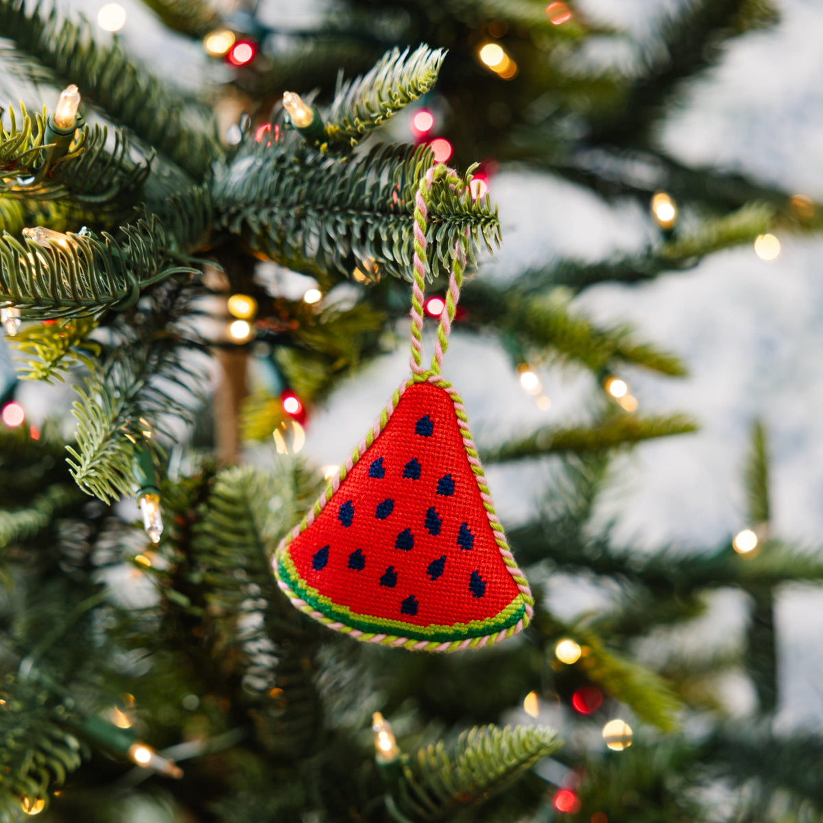 Watermelon needlepoint ornament hanging on a Christmas tree, red triangular slice with blue seeds