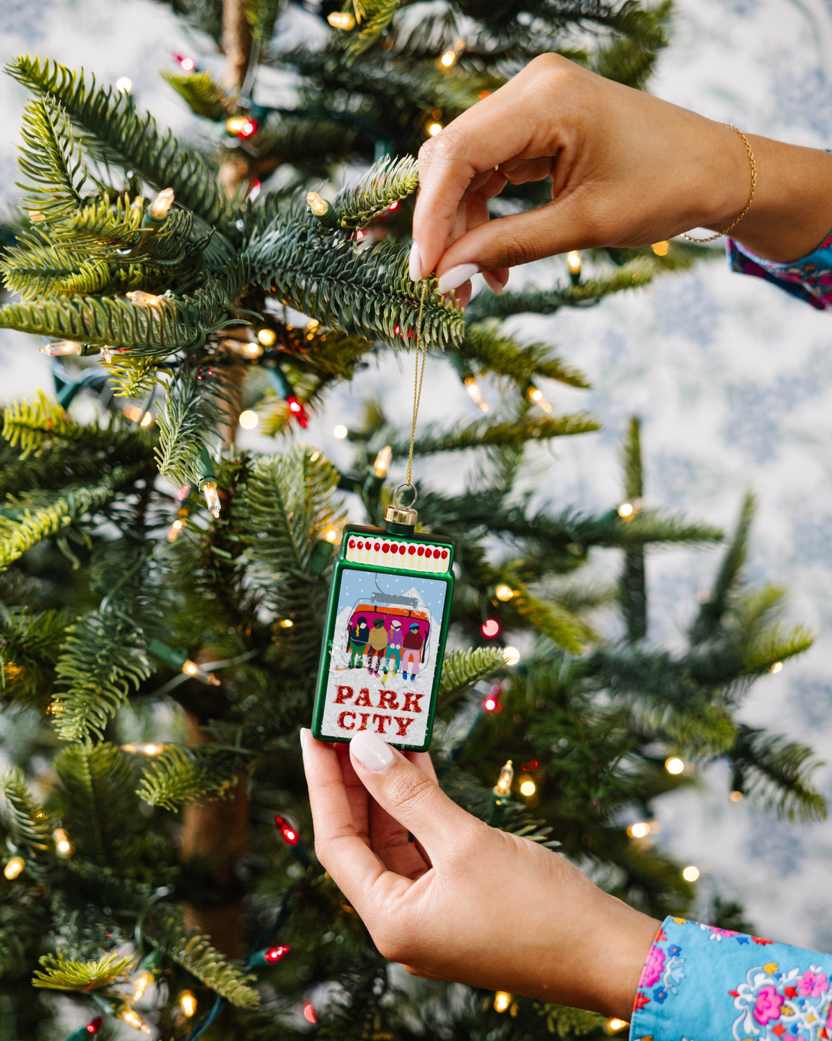 Park City matchbook ornament being hung on evergreen, gold cord, green frame, PARK CITY text.