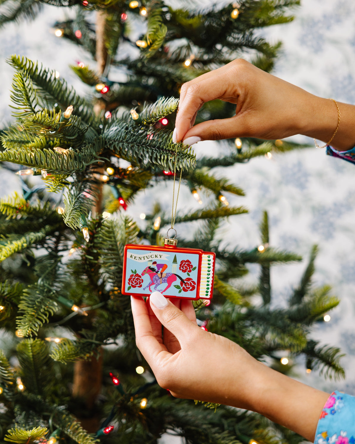 Kentucky matchbook ornament hanging from a tree branch on a gold cord