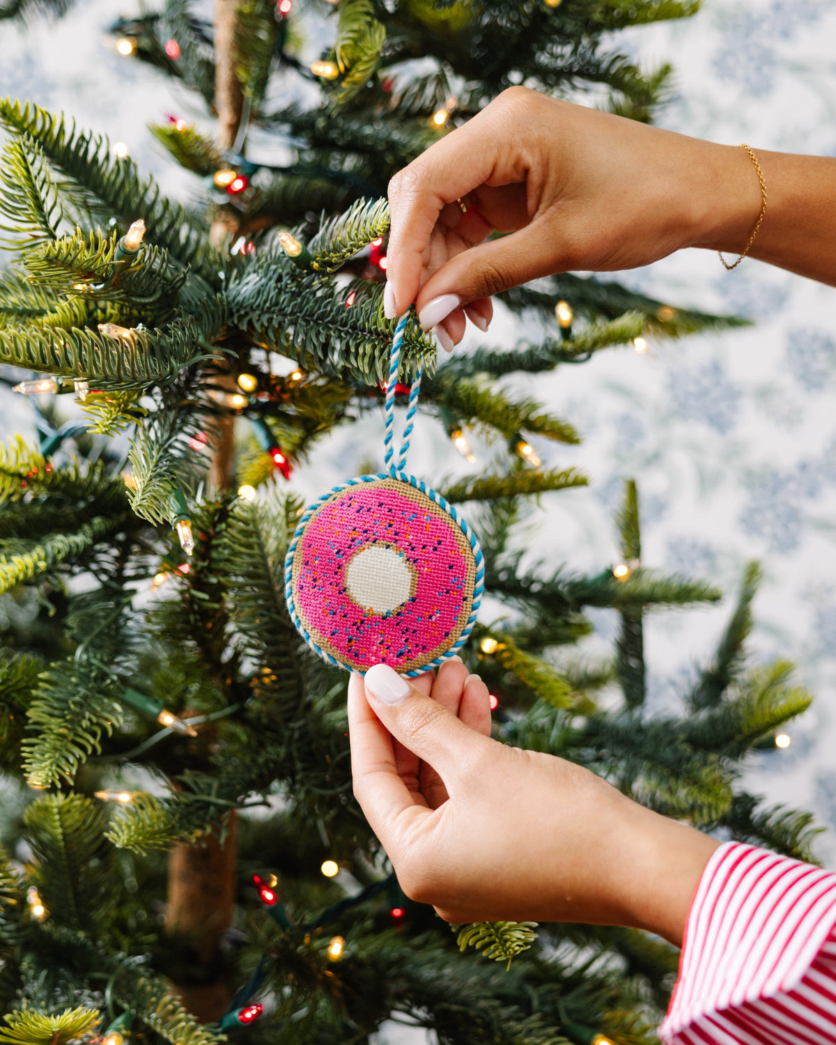 Needlepoint donut ornament with pink needlework, blue trim, white center, hanging from tree
