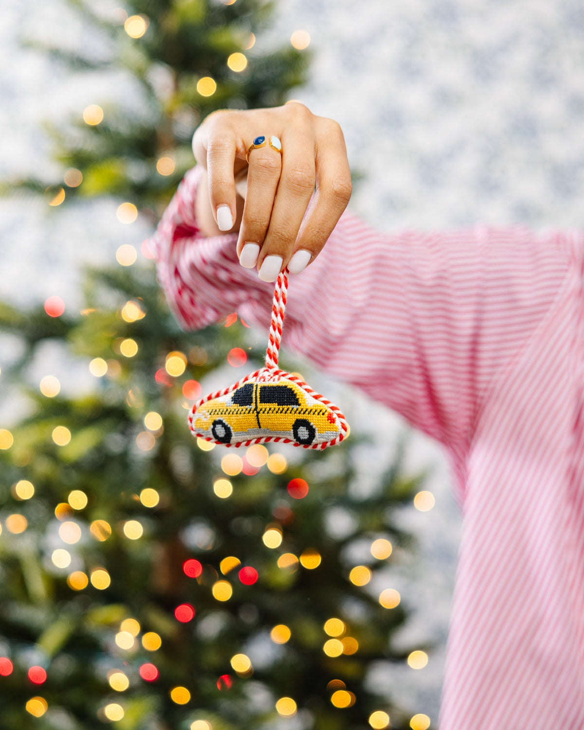 Needlepoint taxi cab ornament held in hand near a decorated Christmas tree