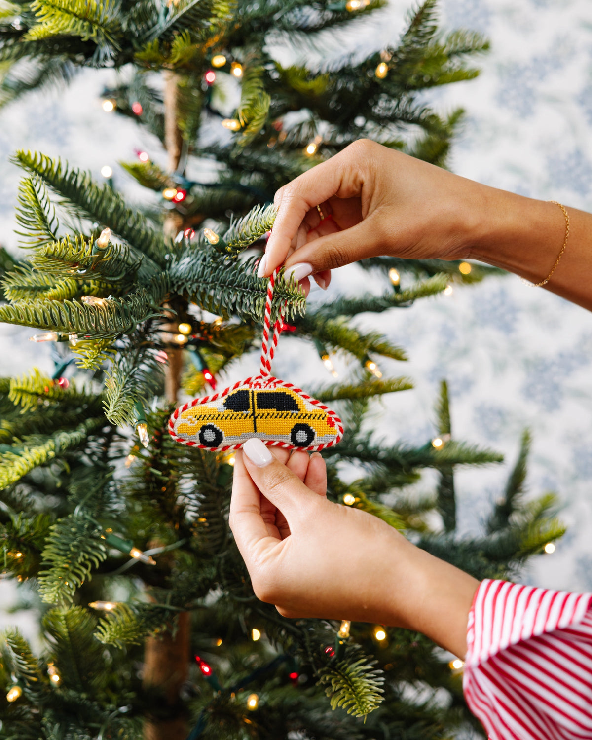 Needlepoint taxi cab ornament being hung on a Christmas tree by hands