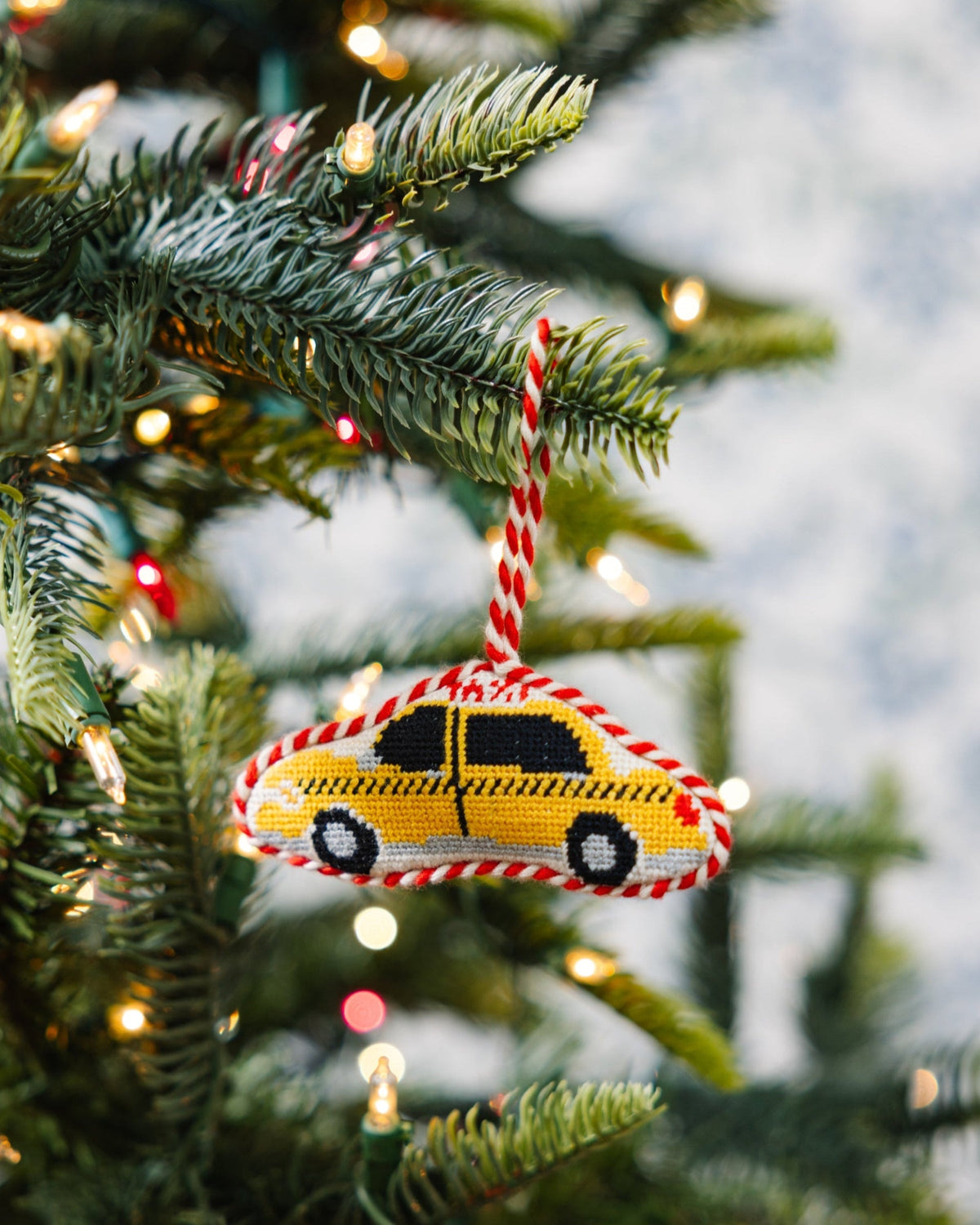 Needlepoint taxi cab ornament hanging on Christmas tree branches