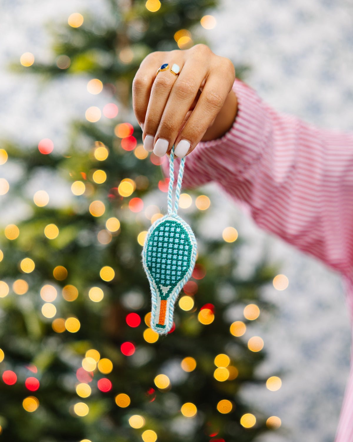 Needlepoint tennis racket ornament suspended from a string, teal with orange handle.