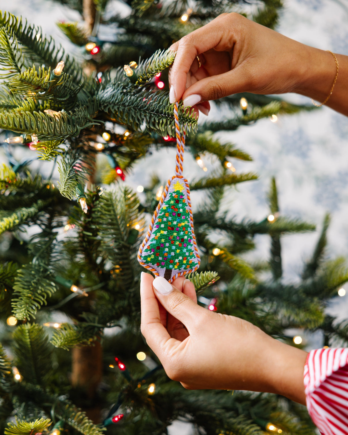 Needlepoint tree ornament being placed on branch, multicolor stitched pattern