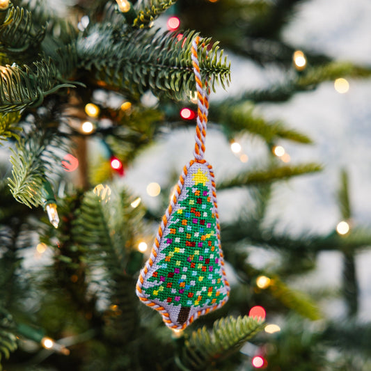 Needlepoint tree ornament hanging on evergreen branch, multicolor stitched pattern