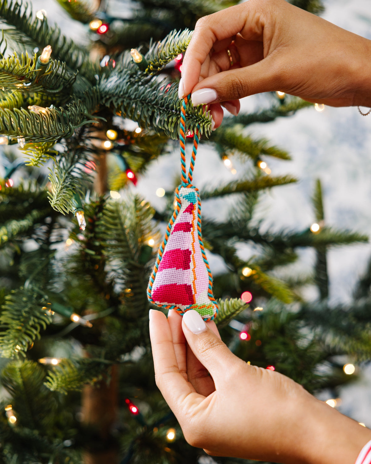 Needlepoint sailboat ornament being hung on a Christmas tree branch