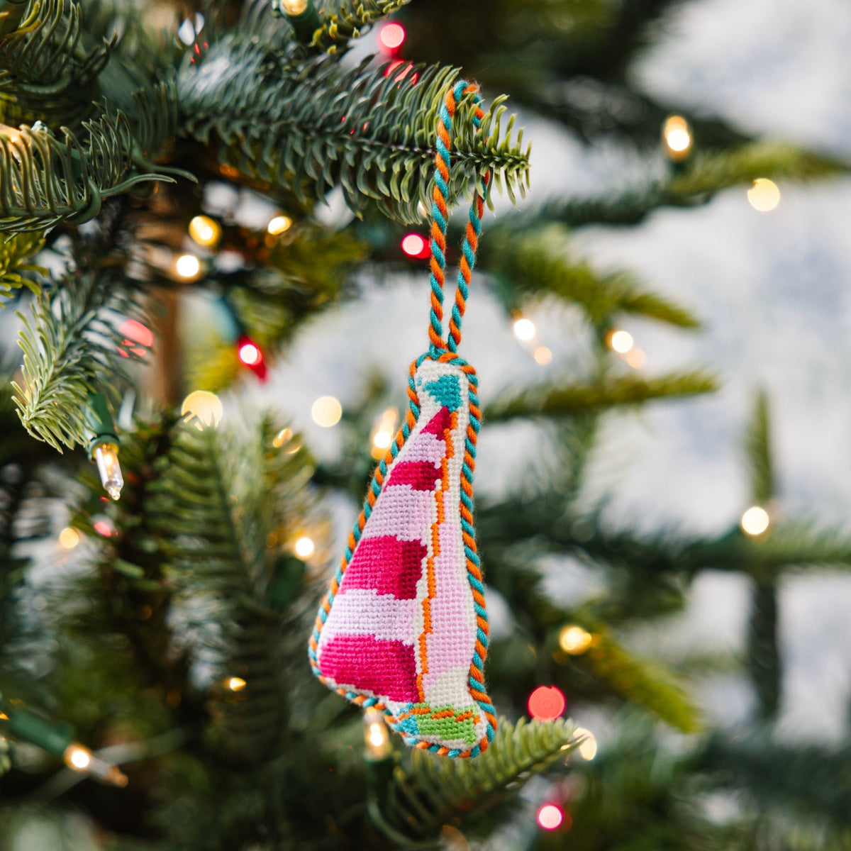 Multicolor needlepoint sailboat ornament hanging on a Christmas tree