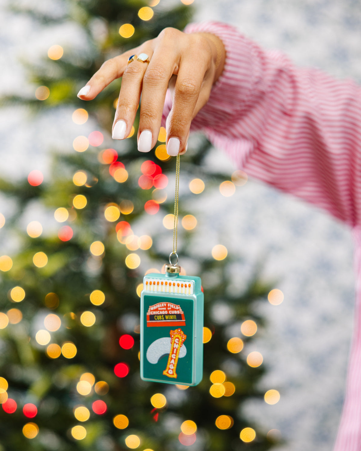 Teal Chicago Cubs matchbook ornament on a string, held in front of lights