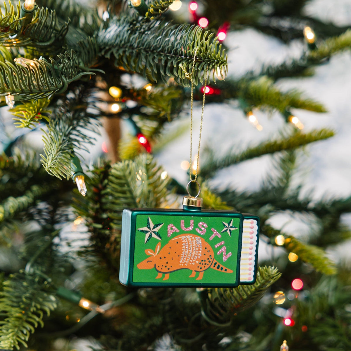 Small green matchbook ornament with Austin branding and gold loop on Christmas tree