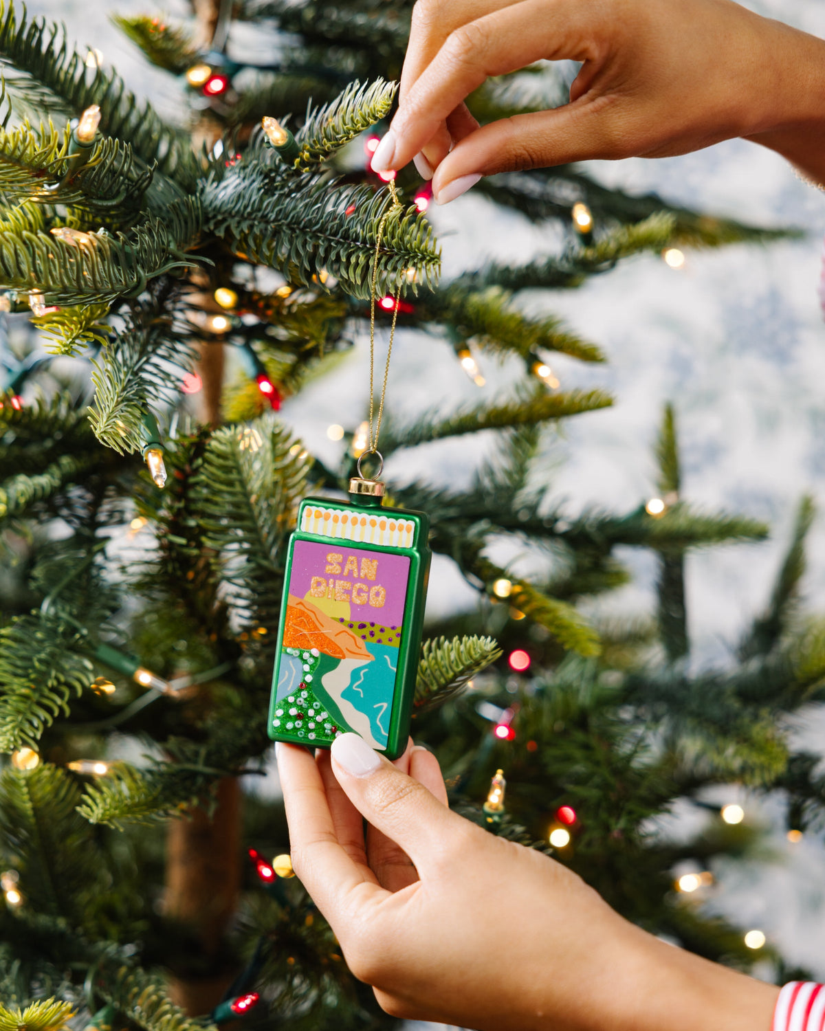 Matchbook ornament with 'SAN DIEGO' artwork held above a Christmas tree