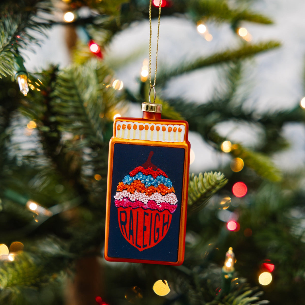 Orange-framed matchbook ornament with Raleigh graphic, hanging from gold cord
