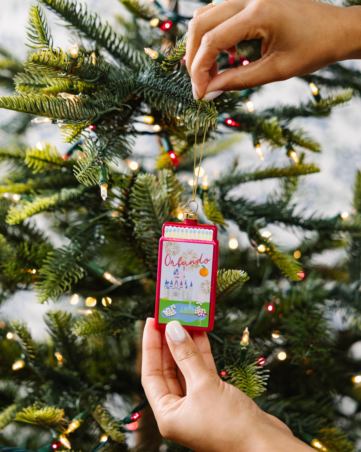 Orlando matchbook ornament being hung on evergreen branch, red frame and cord
