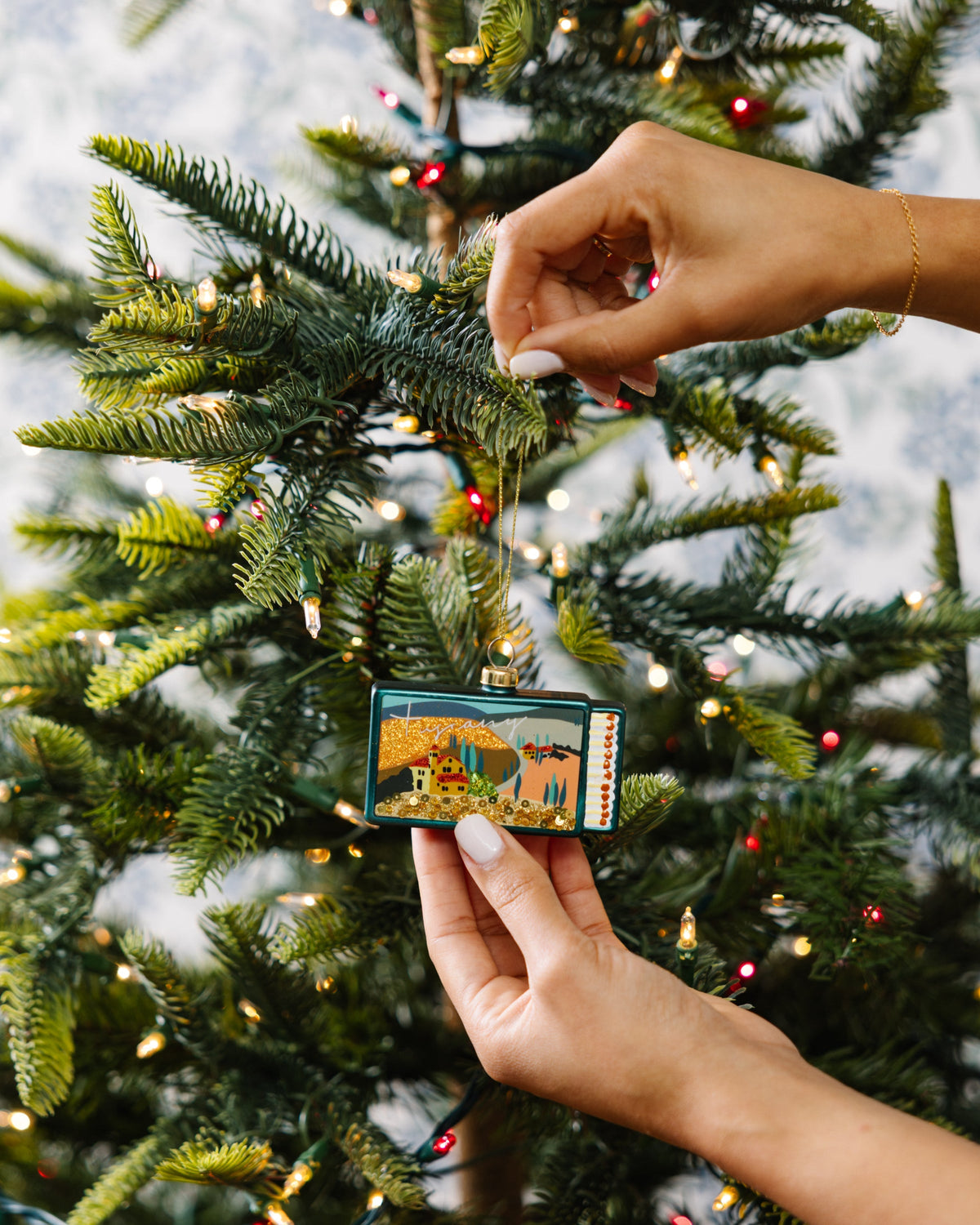 Tuscany matchbook ornament being placed on a tree branch, teal glitter scene and loop