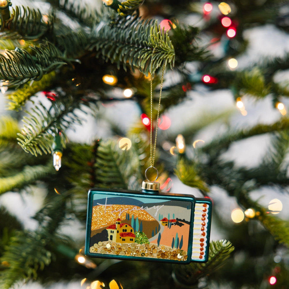 Tuscany matchbook ornament hanging on a Christmas tree, teal glitter landscape design