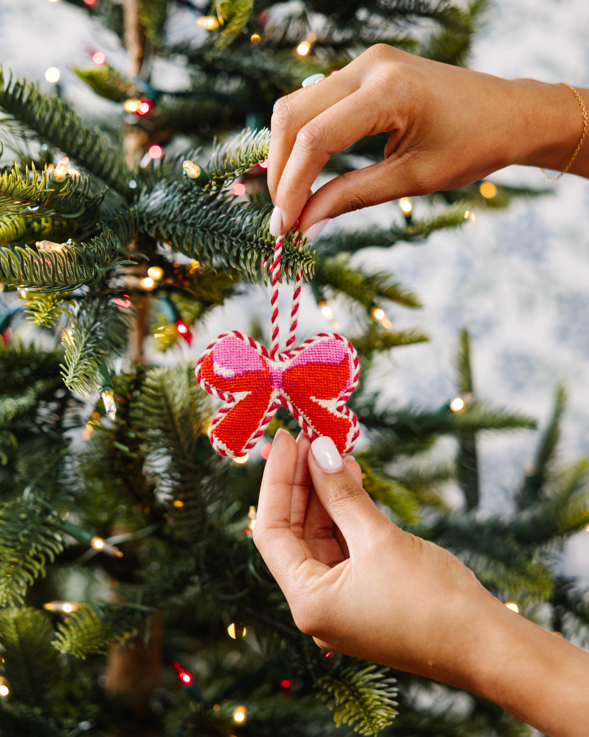 Needlepoint bow ornament being placed on a Christmas tree branch