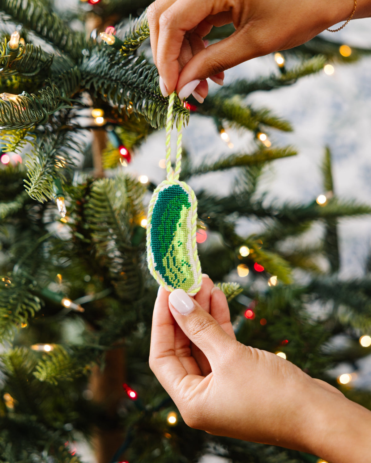 Pickle needlepoint ornament with white cord and green stitched body, held to hang