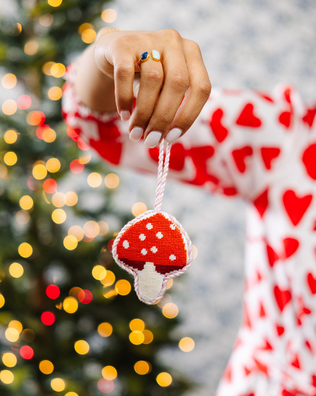 Needlepoint mushroom ornament held by a hand, red cap with white spots and off-white stem