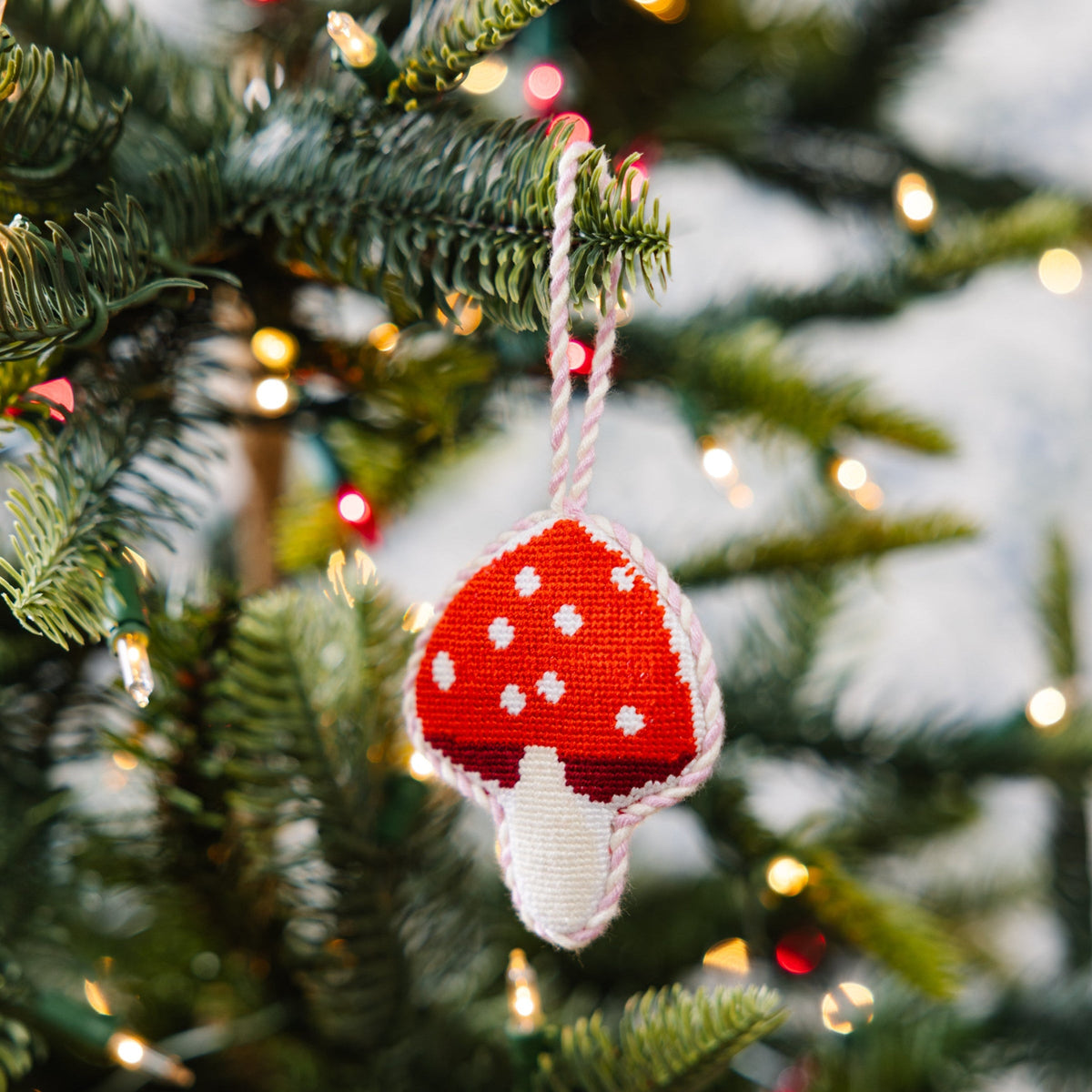 Needlepoint mushroom ornament hanging on a tree, red cap with white spots and stem