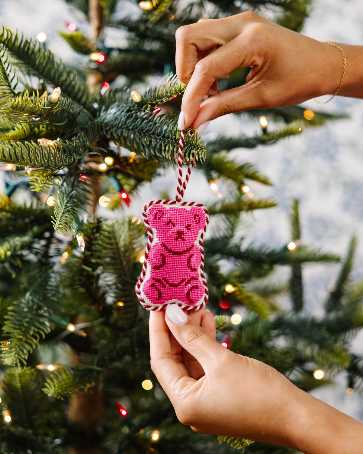 Pink gummy bear needlepoint ornament placed on a Christmas tree branch