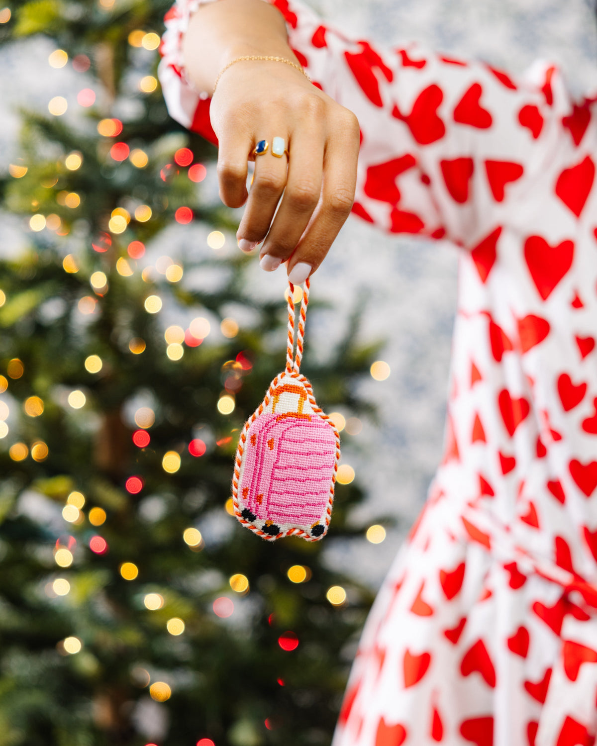 Hand holding pink luggage needlepoint ornament by its braided hanging cord