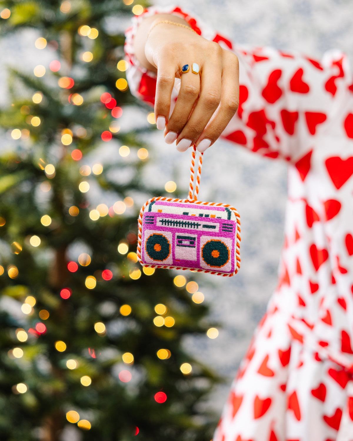 Needlepoint boom box ornament held by hand near a Christmas tree