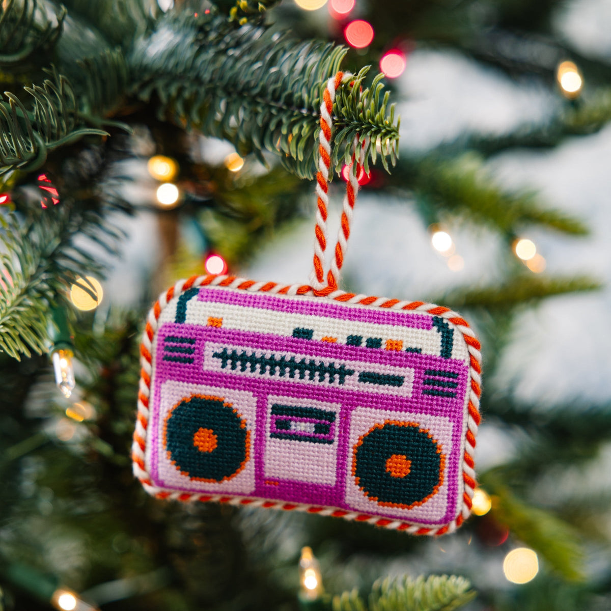 Needlepoint boom box ornament hanging from a Christmas tree branch