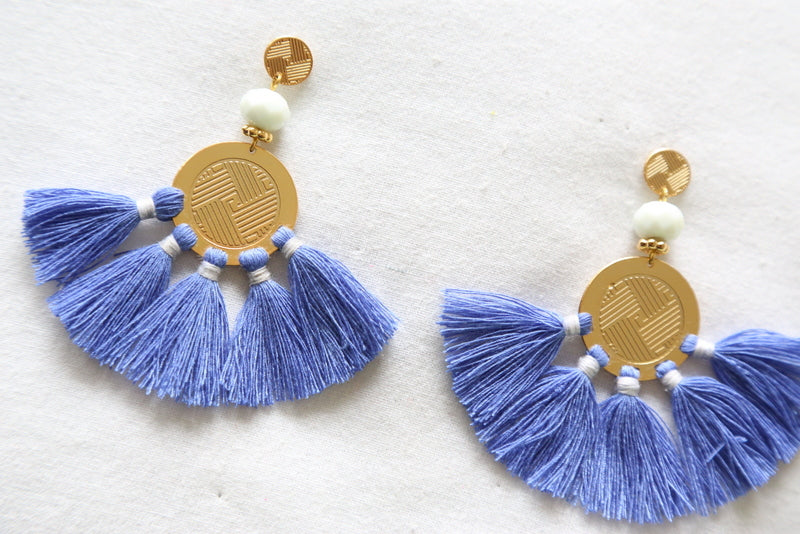 Gold disc and white bead tassel earrings in periwinkle-blue fringe, laid flat