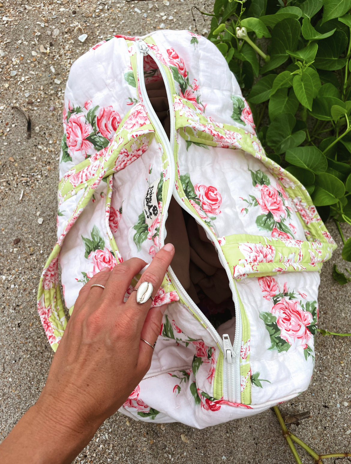 White floral duffle bag with green piping and front zipper, shown open near handle