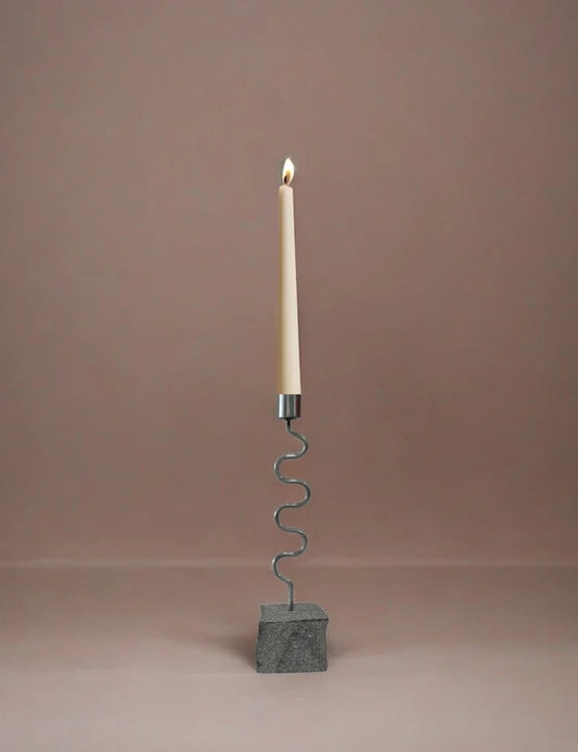 Candle holder with burning white candle on a wavy metal stand and dark gray base block