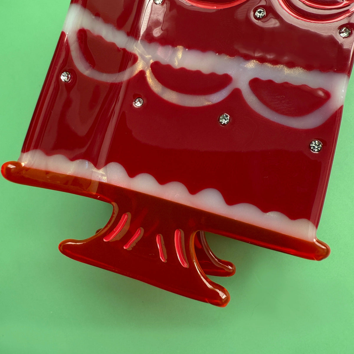 Cake hair claw close-up showing glossy red claw base and front scalloped frosting