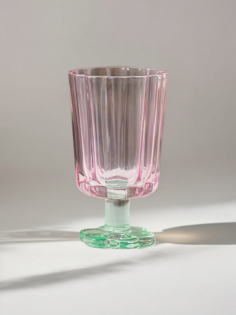 Hand-blown petal goblet glass, clear with pink tint, on green flared base.
