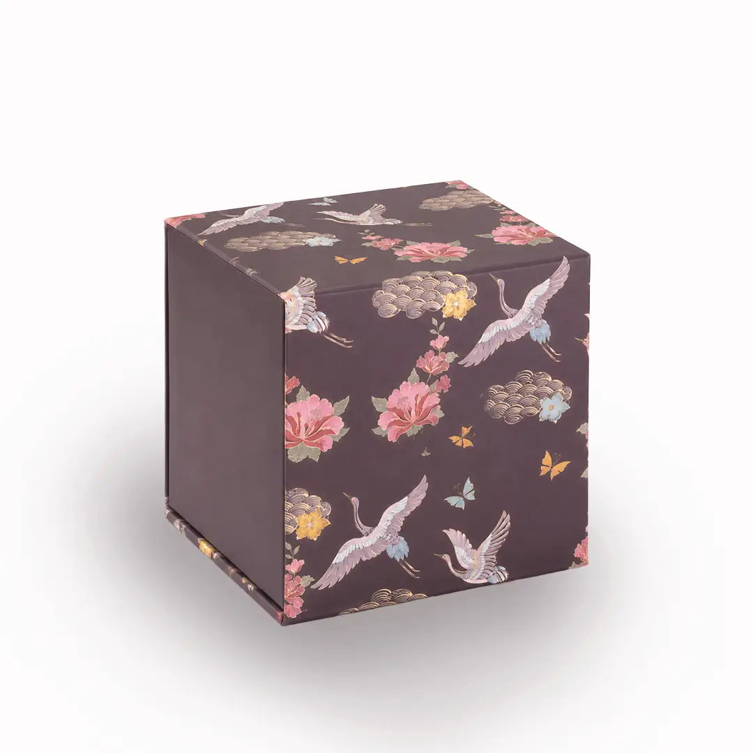 Square gift box in dark brown with floral and crane pattern, “mela” logo on side
