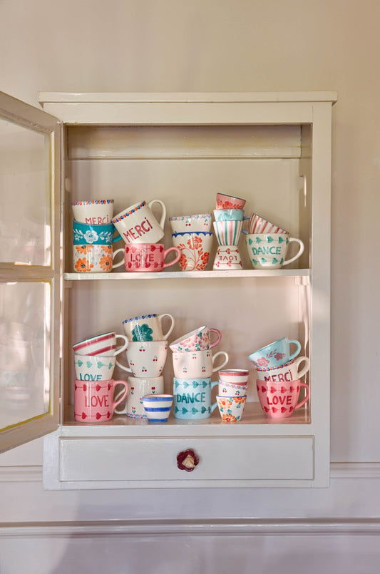 Ceramic tea cups with hand-painted floral designs on display shelf in a cabinet