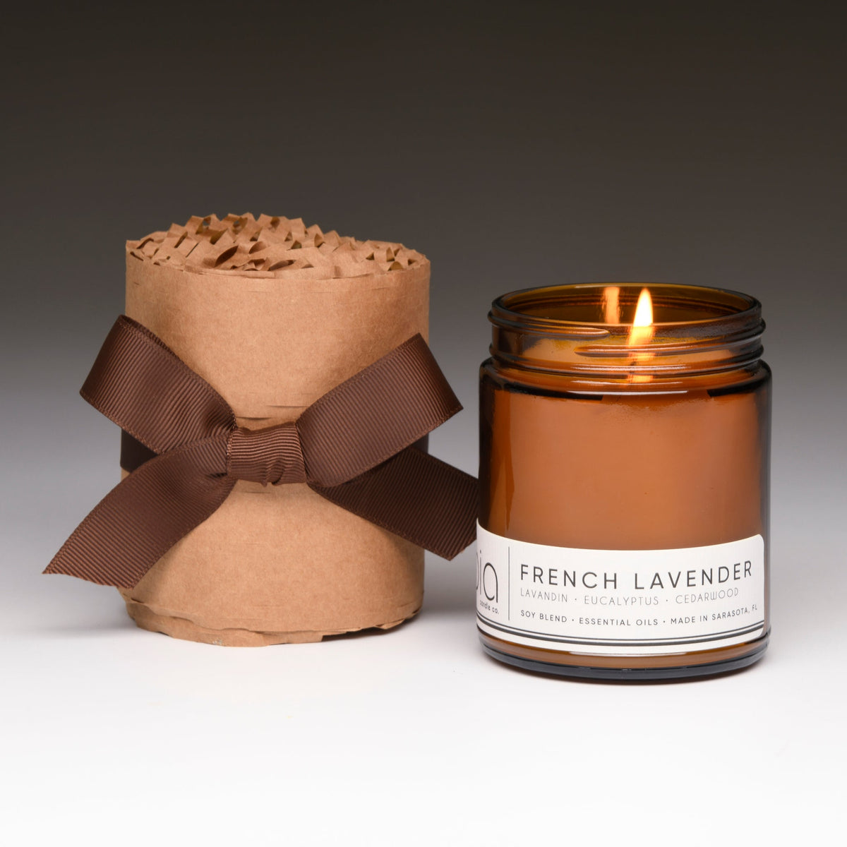 Amber soy candle with lit wick, kraft wrap gift with brown ribbon bow