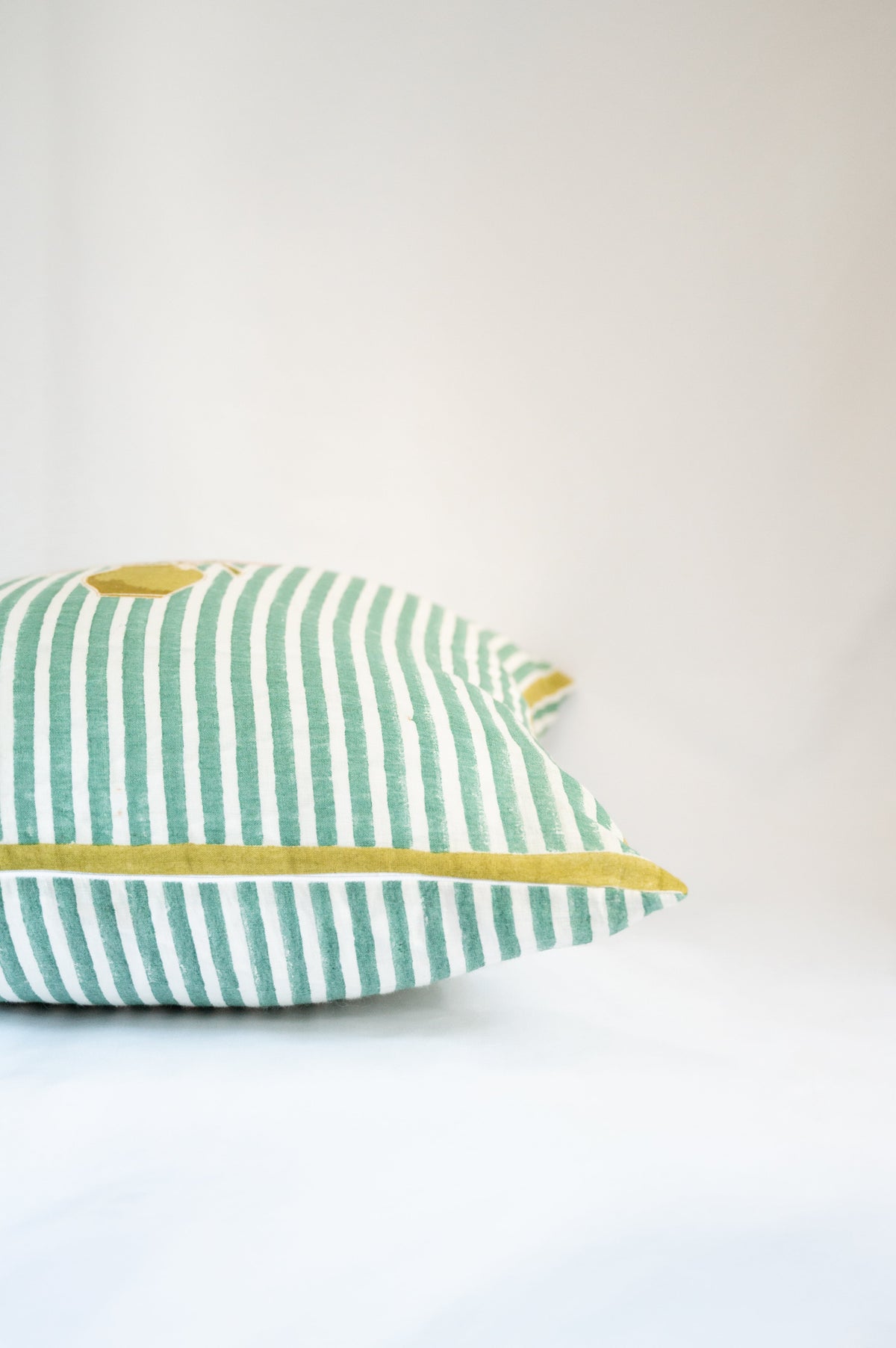 Corner view of green striped decorative pillow with floral bouquet applique and yellow piping
