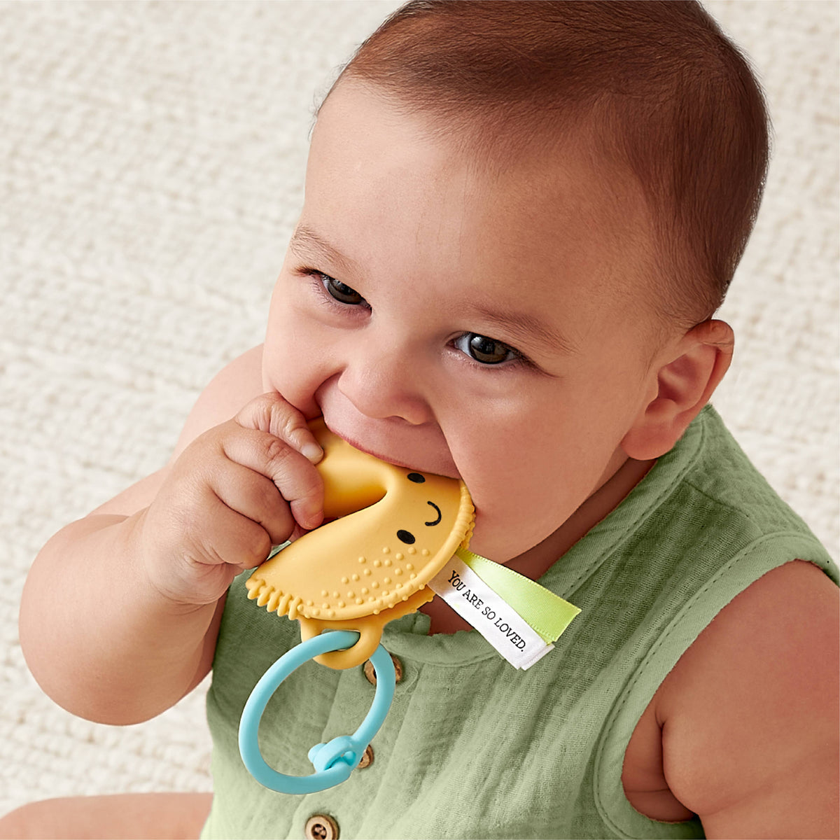Baby toddler holding a fortune-cookie silicone teether with blue teething ring