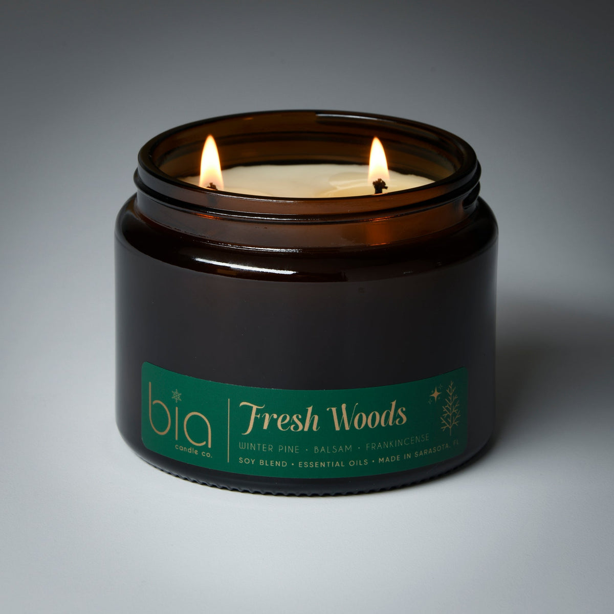 Black glass candle jar with lit wick and green Fresh Woods label