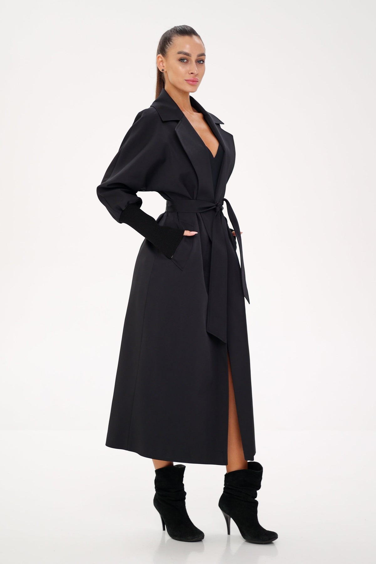 Black belted trench coat shown from the side, with a long split front