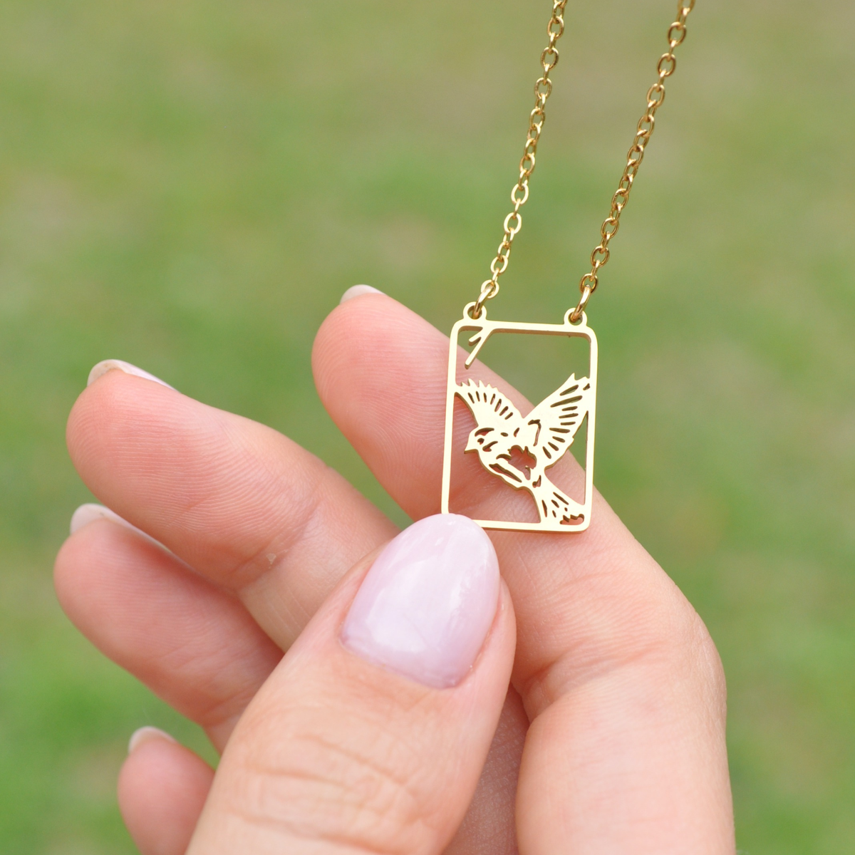 Gold square bird pendant necklace held in hand, thin chain