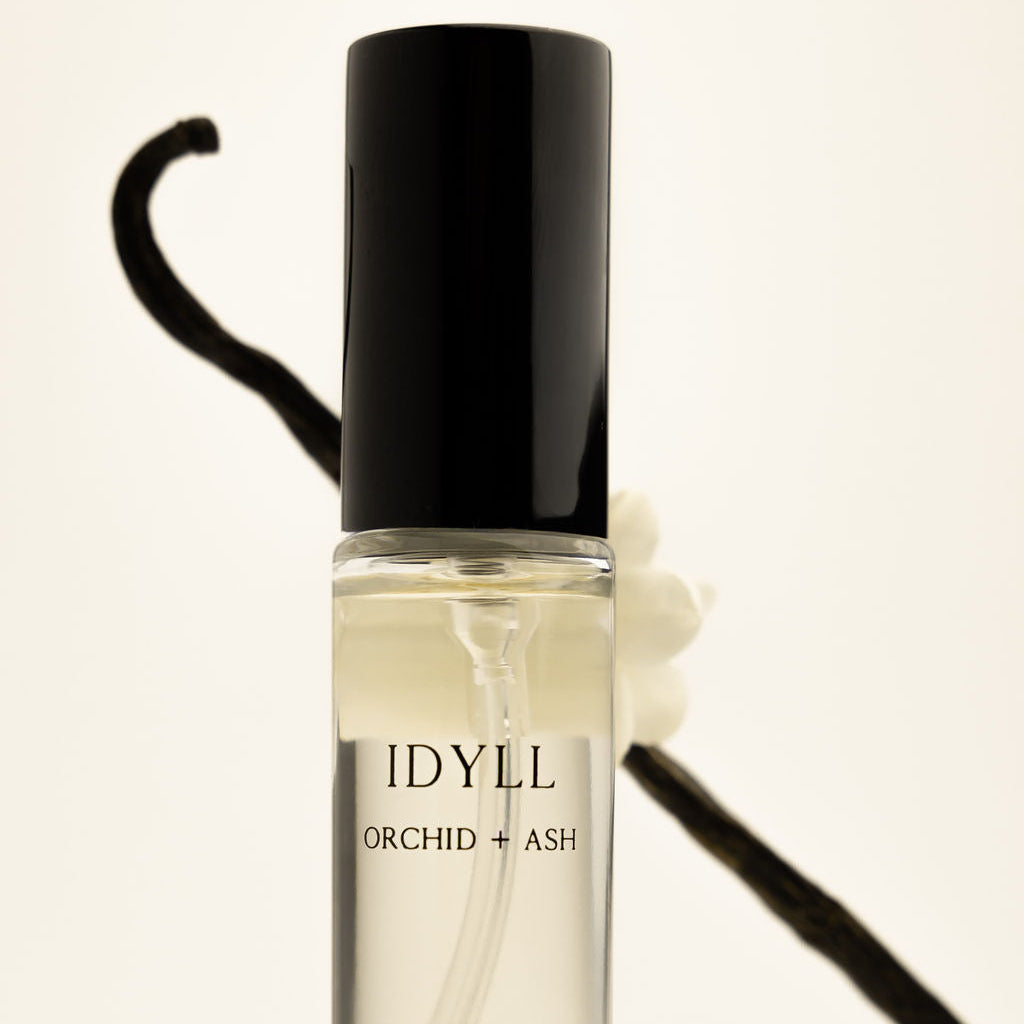 Clear perfume bottle with black cap labeled IDYLL ORCHID + ASH